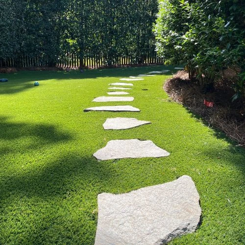 a green artificial turf lawn next to a custom-made flagstone walkway